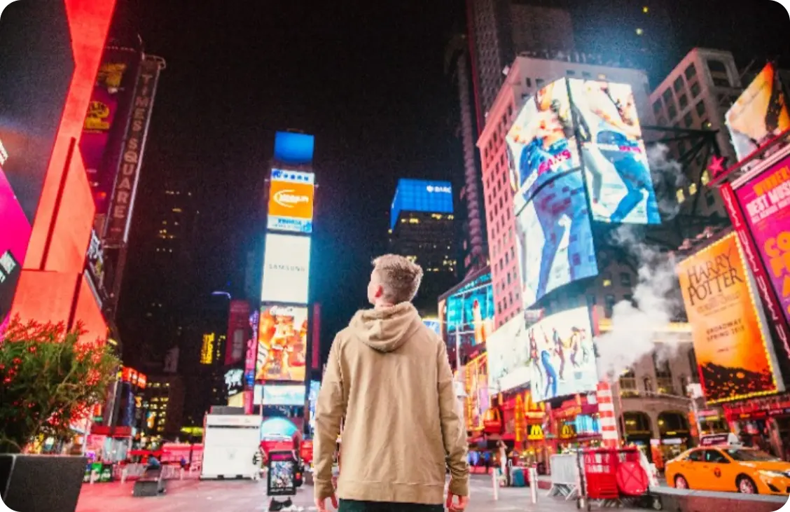 A man standing in the middle of bustling city full of digital signages